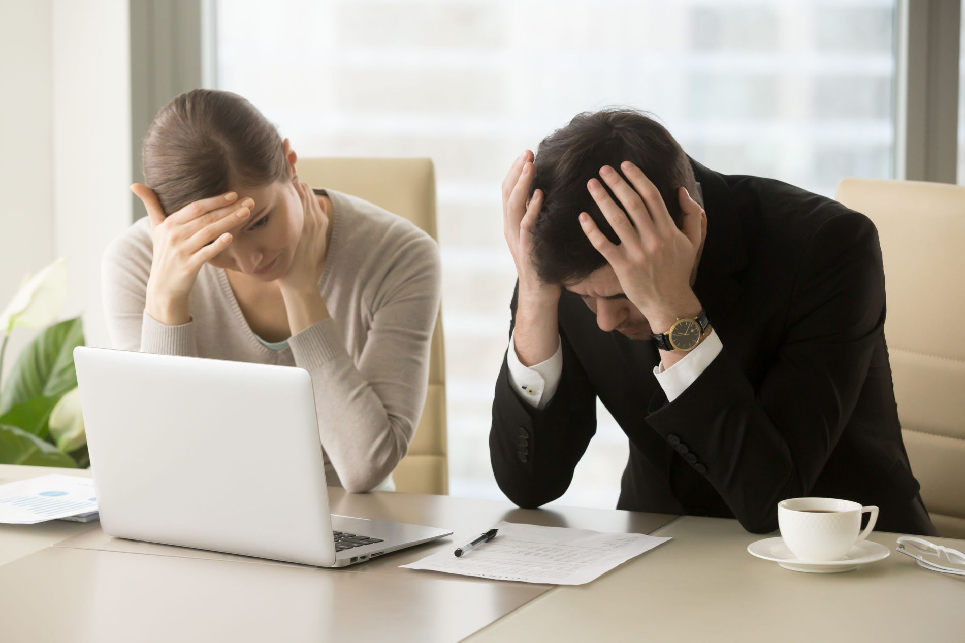 Tired frustrated business people feeling stressed, upset executives sitting near laptop, holding head in hands, worried about business problem failure, depressed by bad news, company bankruptcy
