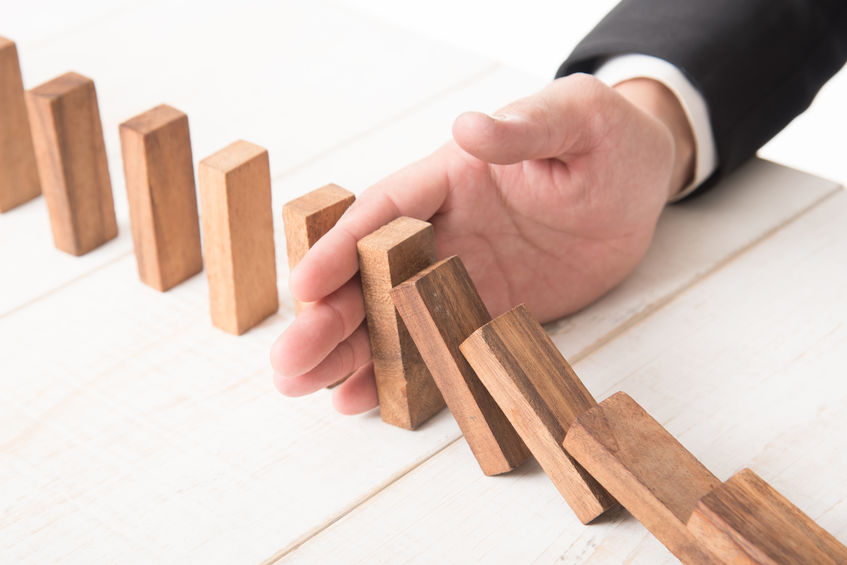 Businessman hand trying to stop toppling dominoes on wood,stop domino effect